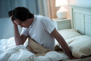 Young man with hand in hair suffering from headache in bed